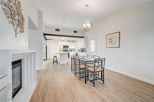 6771 Shelter Ln, Las Vegas, NV 89103 - dining space with light wood-type flooring, a chandelier, baseboards, and a glass covered fireplace