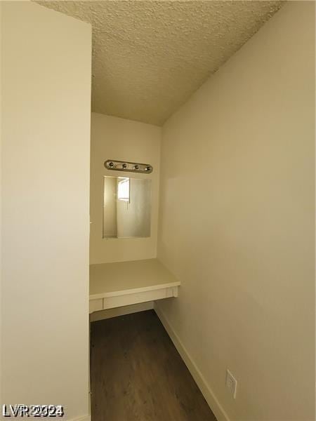 hallway featuring baseboards, wood finished floors, and a textured ceiling