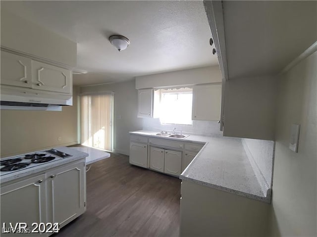 kitchen featuring under cabinet range hood, a sink, white stovetop, white cabinetry, and dark wood-type flooring