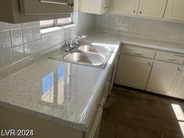 kitchen with a sink, decorative backsplash, white cabinets, dark wood finished floors, and light stone counters
