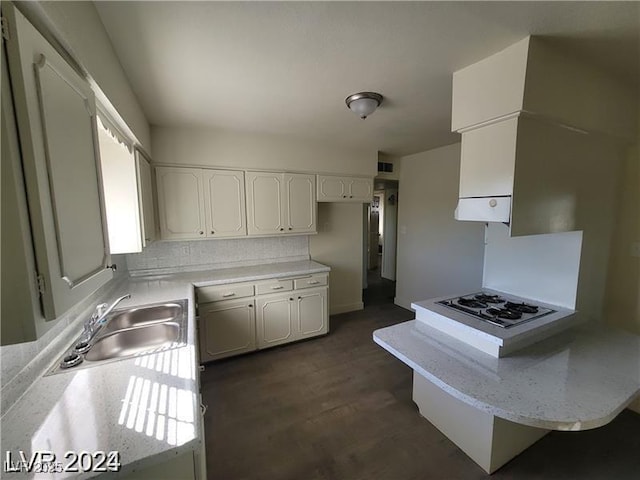 kitchen featuring a peninsula, a sink, gas cooktop, white cabinets, and light countertops