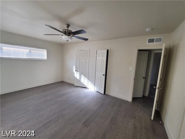 unfurnished bedroom featuring dark wood finished floors, two closets, baseboards, and ceiling fan