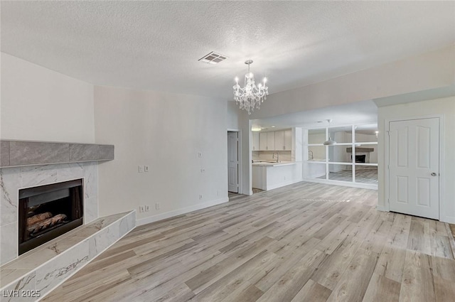 2633 S Durango Dr Unit 201, Las Vegas, NV 89117 - unfurnished living room with a fireplace, light wood-style floors, a chandelier, a textured ceiling, and baseboards