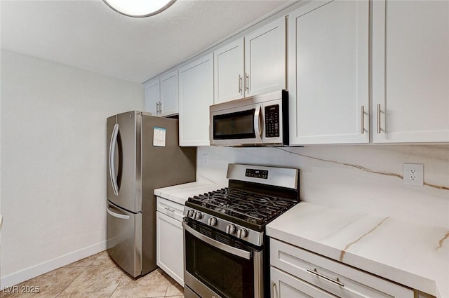 2633 S Durango Dr Unit 201, Las Vegas, NV 89117 - kitchen with appliances with stainless steel finishes, baseboards, white cabinetry, light tile patterned floors, and light stone countertops
