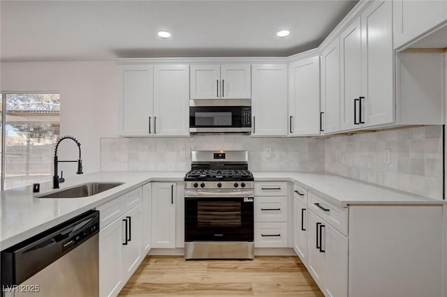 kitchen with appliances with stainless steel finishes, a sink, white cabinets, light wood-style floors, and recessed lighting