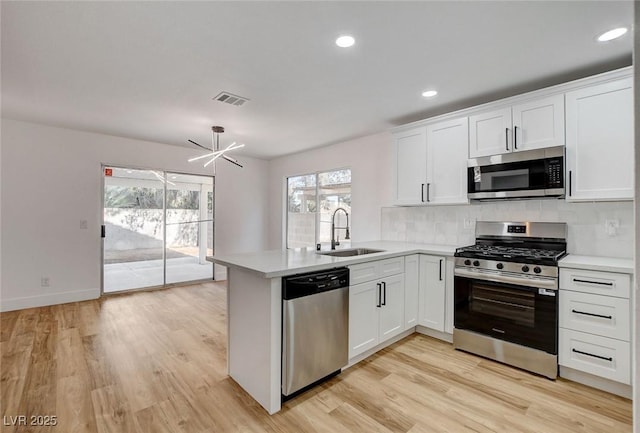 kitchen featuring appliances with stainless steel finishes, a sink, a peninsula, light countertops, and decorative backsplash