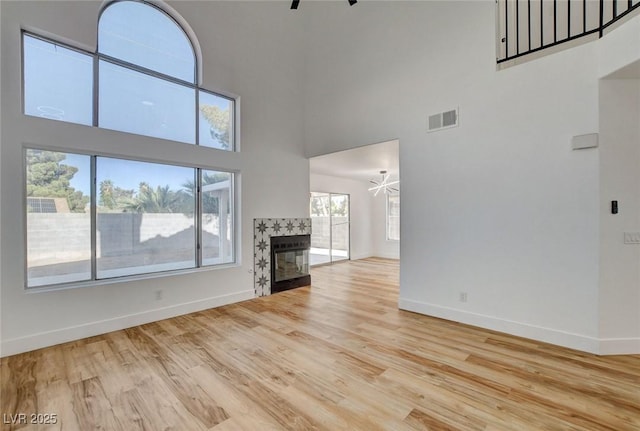 unfurnished living room with a high ceiling, baseboards, wood finished floors, ceiling fan, and a fireplace
