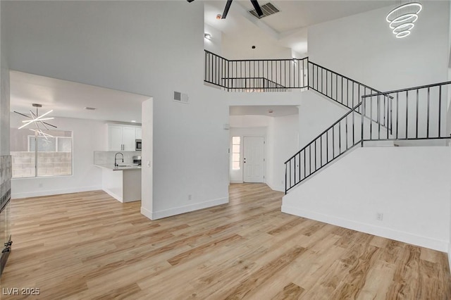 unfurnished living room with stairs, ceiling fan, light wood-type flooring, a high ceiling, and baseboards