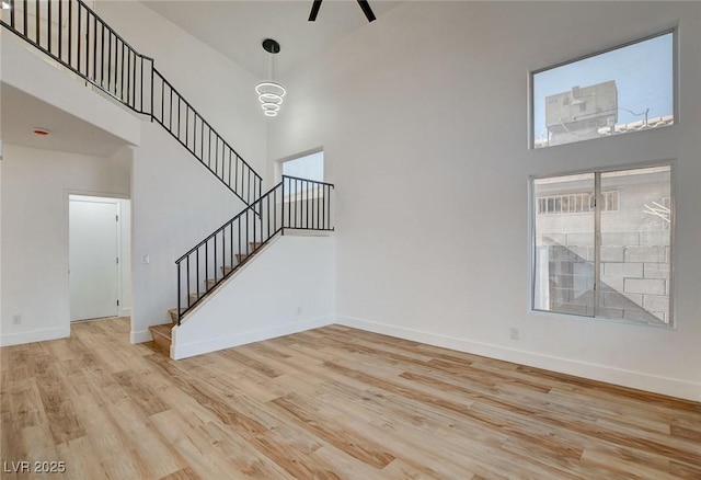 unfurnished living room with a towering ceiling, light wood-type flooring, stairs, and baseboards