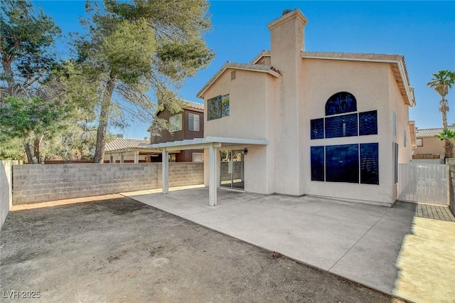 rear view of house featuring stucco siding, a patio, fence, a chimney, and a tiled roof