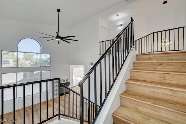 staircase featuring a high ceiling, ceiling fan, and wood finished floors