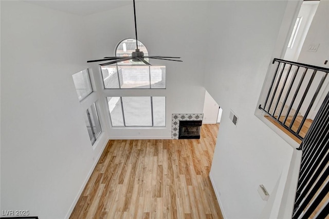 unfurnished living room featuring light wood-style floors, a towering ceiling, stairs, baseboards, and a fireplace