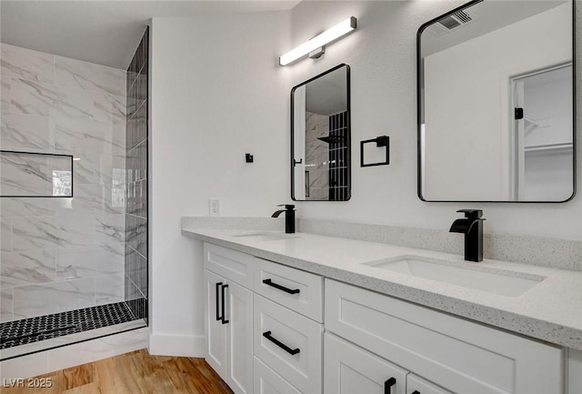bathroom with a marble finish shower, double vanity, wood finished floors, and baseboards
