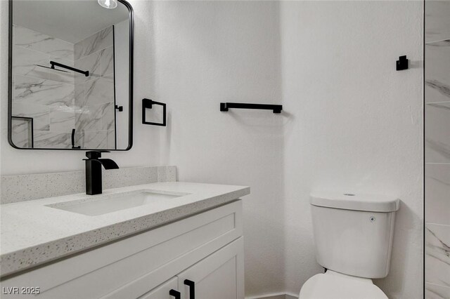 bathroom featuring toilet, a marble finish shower, and vanity