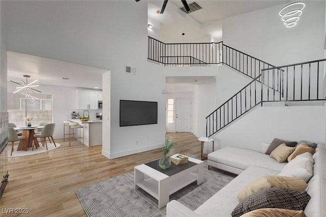 living room featuring stairs, a high ceiling, light wood finished floors, a ceiling fan, and baseboards