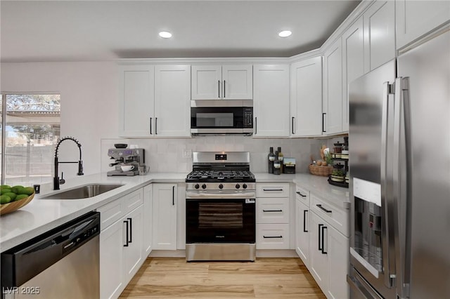 kitchen with stainless steel appliances, a sink, light countertops, white cabinets, and recessed lighting