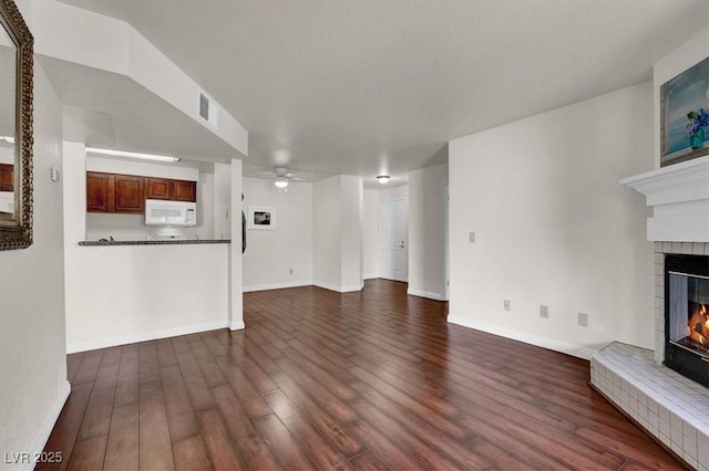 unfurnished living room with a brick fireplace, a ceiling fan, dark wood-style floors, and baseboards