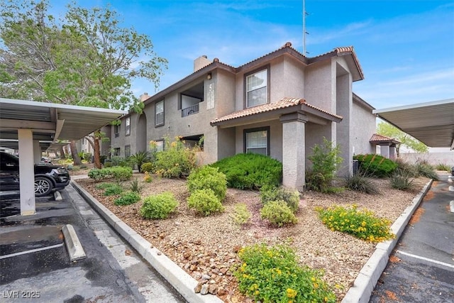 view of side of property featuring stucco siding, covered and uncovered parking, a chimney, and a tile roof