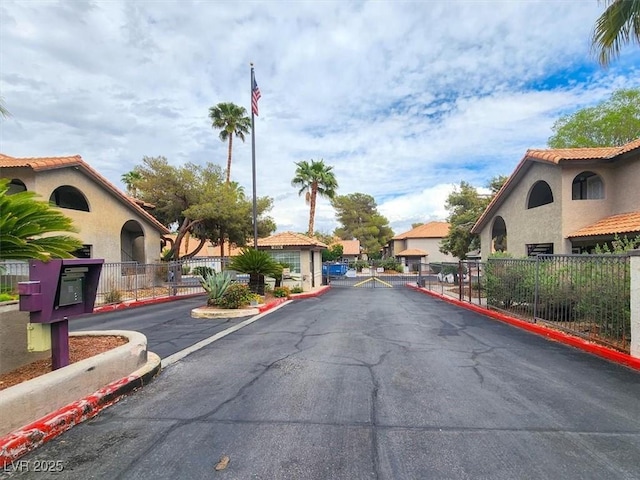 view of asphalt road with a gate, curbs, a gated entry, and a residential view