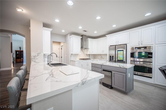 11112 Pine Greens Ct, Las Vegas, NV 89144 - kitchen with a sink, appliances with stainless steel finishes, wall chimney exhaust hood, arched walkways, and light stone countertops