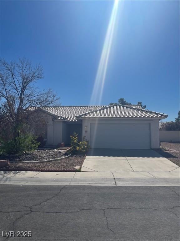 ranch-style house featuring a tiled roof, driveway, an attached garage, and stucco siding