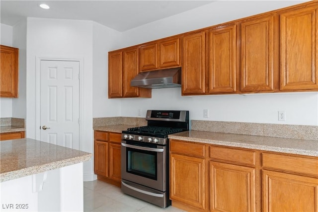 kitchen featuring gas stove, under cabinet range hood, brown cabinets, light stone counters, and recessed lighting