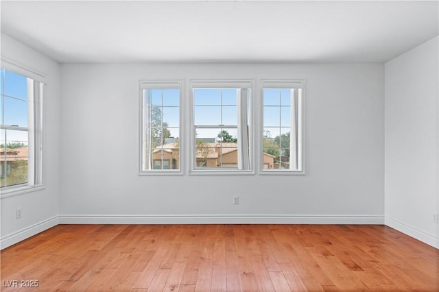 spare room featuring plenty of natural light, light wood-style flooring, and baseboards