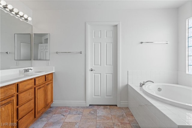 bathroom featuring baseboards, a garden tub, vanity, and stone finish floors