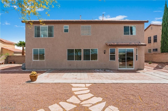 rear view of house with fence, a tiled roof, stucco siding, and a patio area