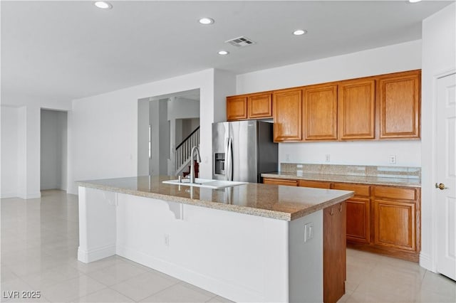 kitchen with stainless steel fridge with ice dispenser, a sink, brown cabinets, recessed lighting, and a kitchen island with sink