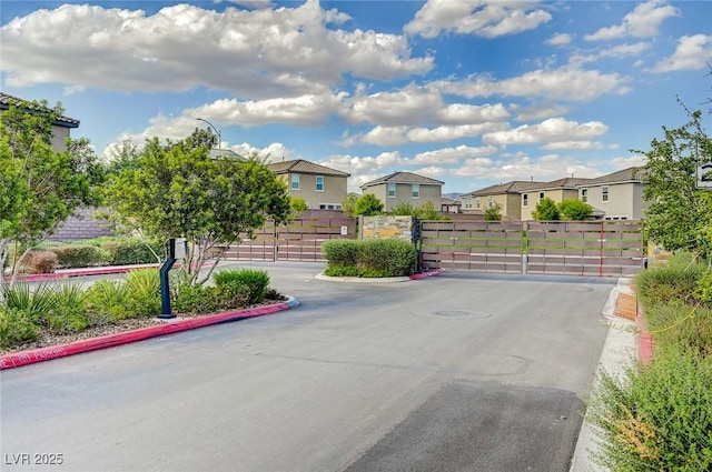 view of asphalt road with a residential view, a gate, a gated entry, curbs, and street lights