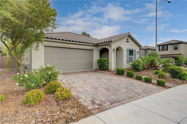 mediterranean / spanish house with stucco siding, decorative driveway, an attached garage, and a tiled roof