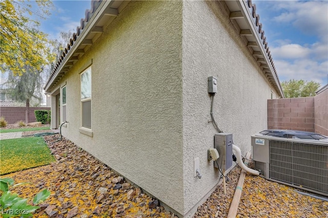 view of side of property with stucco siding, central AC, and fence