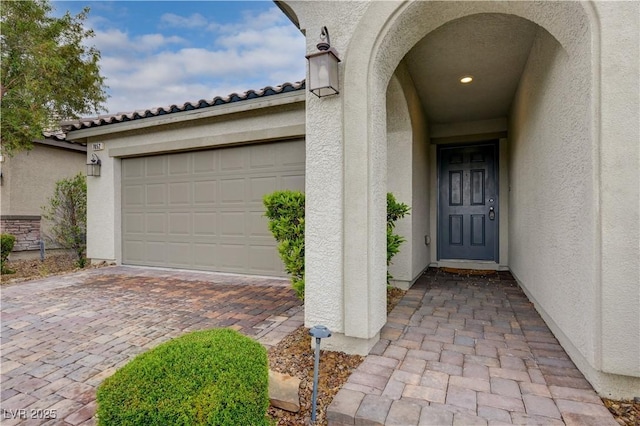entrance to property featuring stucco siding, decorative driveway, and an attached garage