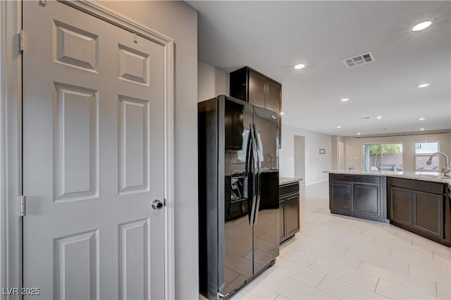 kitchen featuring black refrigerator with ice dispenser, dark brown cabinetry, light stone countertops, light tile patterned floors, and recessed lighting