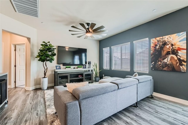 living room featuring a ceiling fan, light wood-type flooring, baseboards, and a fireplace