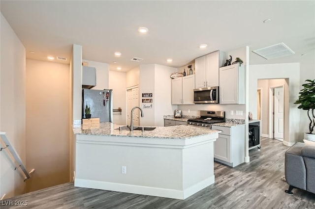 kitchen featuring stainless steel appliances, a sink, wood finished floors, a peninsula, and light stone countertops