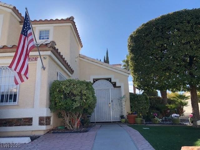 view of home's exterior with a tiled roof, stucco siding, and a gate