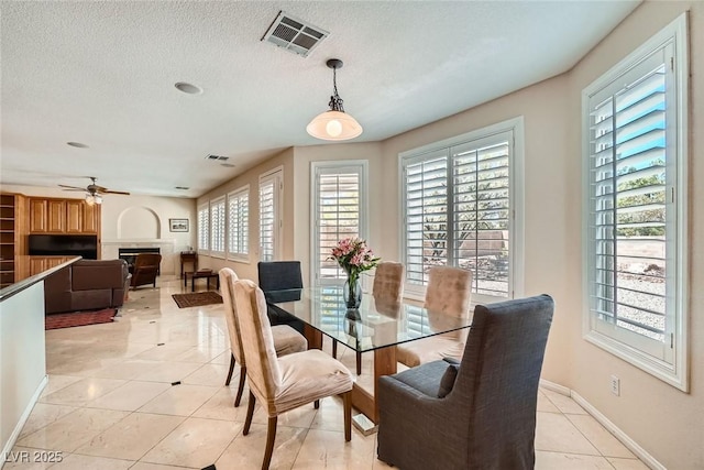 dining room featuring a glass covered fireplace, healthy amount of natural light, baseboards, light tile patterned flooring, and a textured ceiling