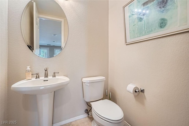 half bathroom featuring toilet, tile patterned floors, a sink, and baseboards