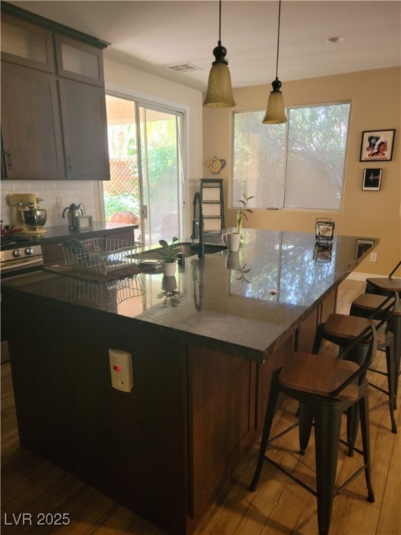 kitchen with wood finished floors, a kitchen bar, backsplash, glass insert cabinets, and hanging light fixtures