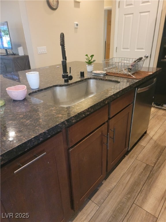 kitchen with a sink, dishwasher, light wood-style flooring, and dark stone counters
