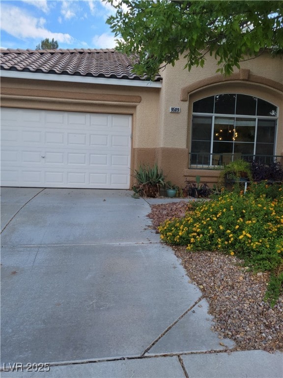 view of front of home featuring driveway, stucco siding, a garage, and a tiled roof