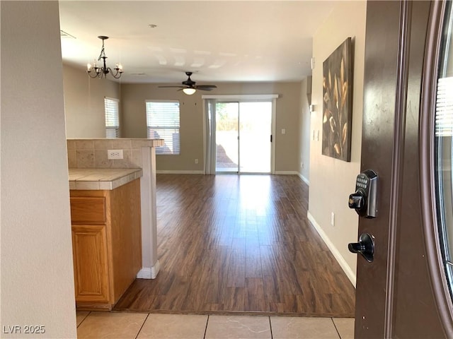 interior space with a ceiling fan, baseboards, light wood-type flooring, and a chandelier