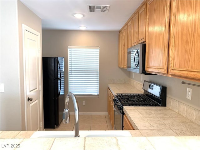 kitchen with stainless steel appliances, tile countertops, light tile patterned floors, a sink, and baseboards
