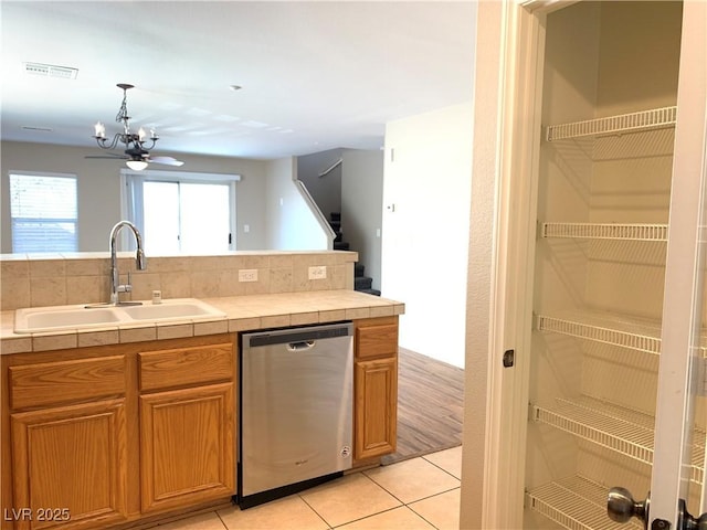 kitchen with stainless steel dishwasher, a sink, tile counters, and a chandelier