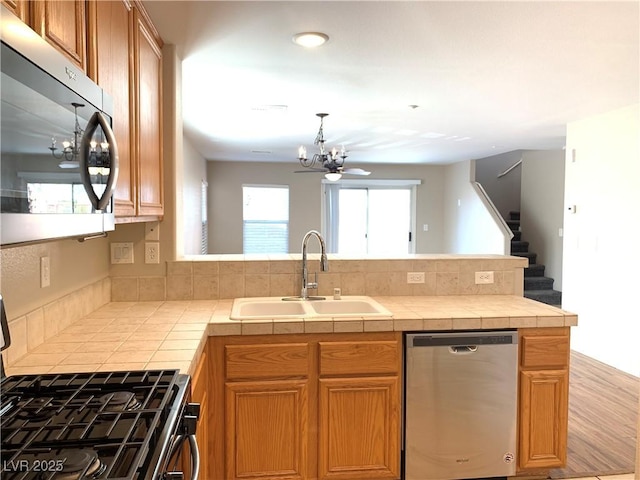 kitchen featuring stainless steel appliances, a sink, a chandelier, a peninsula, and tile countertops