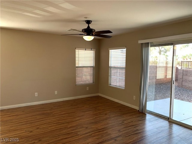 unfurnished room with dark wood finished floors, healthy amount of natural light, a ceiling fan, and baseboards