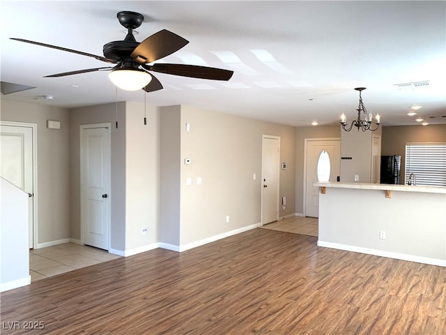 unfurnished living room featuring light wood-type flooring, ceiling fan, baseboards, and a chandelier