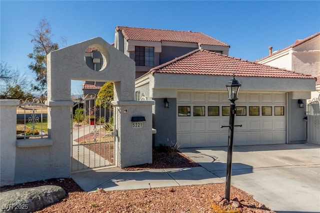 mediterranean / spanish home featuring concrete driveway, a tile roof, an attached garage, stucco siding, and a gate